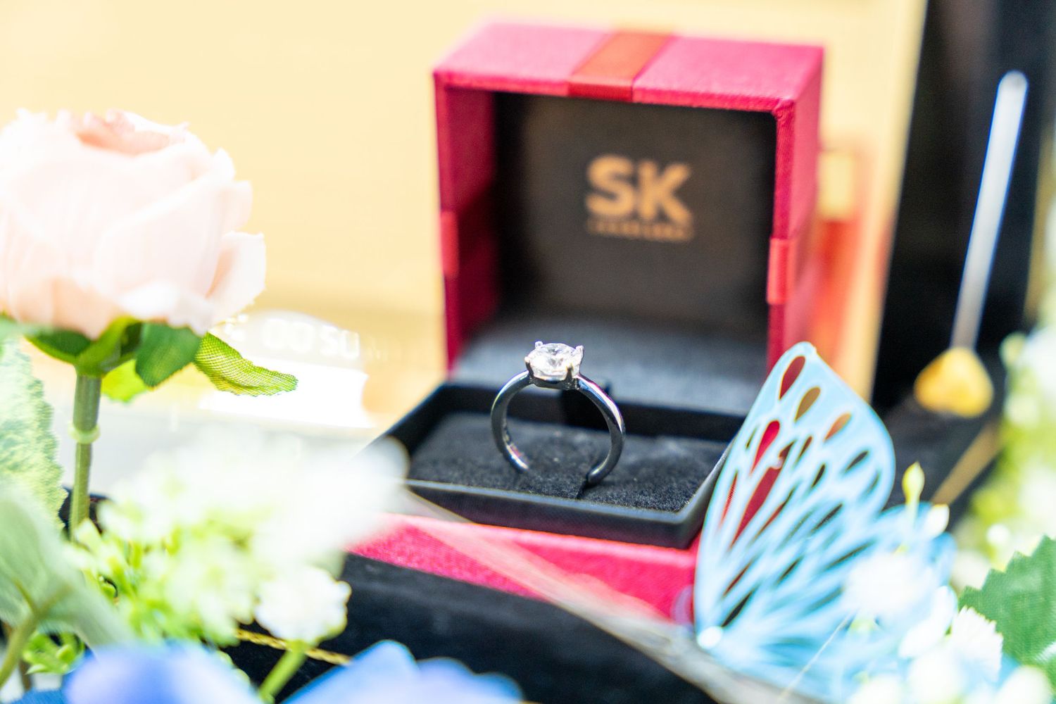 Engagement ring in red SK jewelry box with rose and butterfly decor.