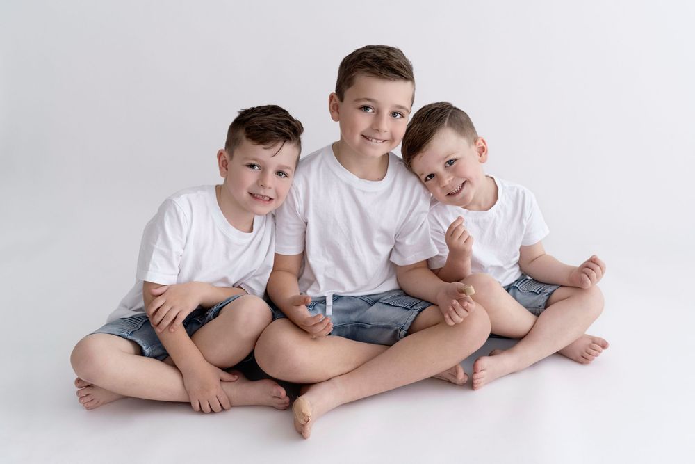 Three brothers in white shirts sitting together on a white background