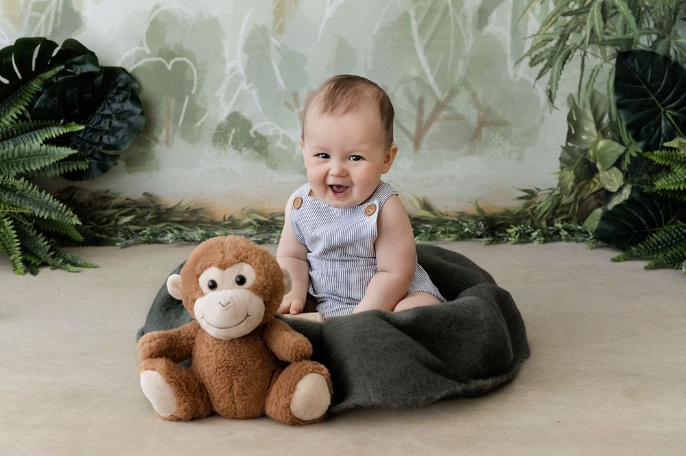 Baby sitting in a dark green bowl with a toy monkey