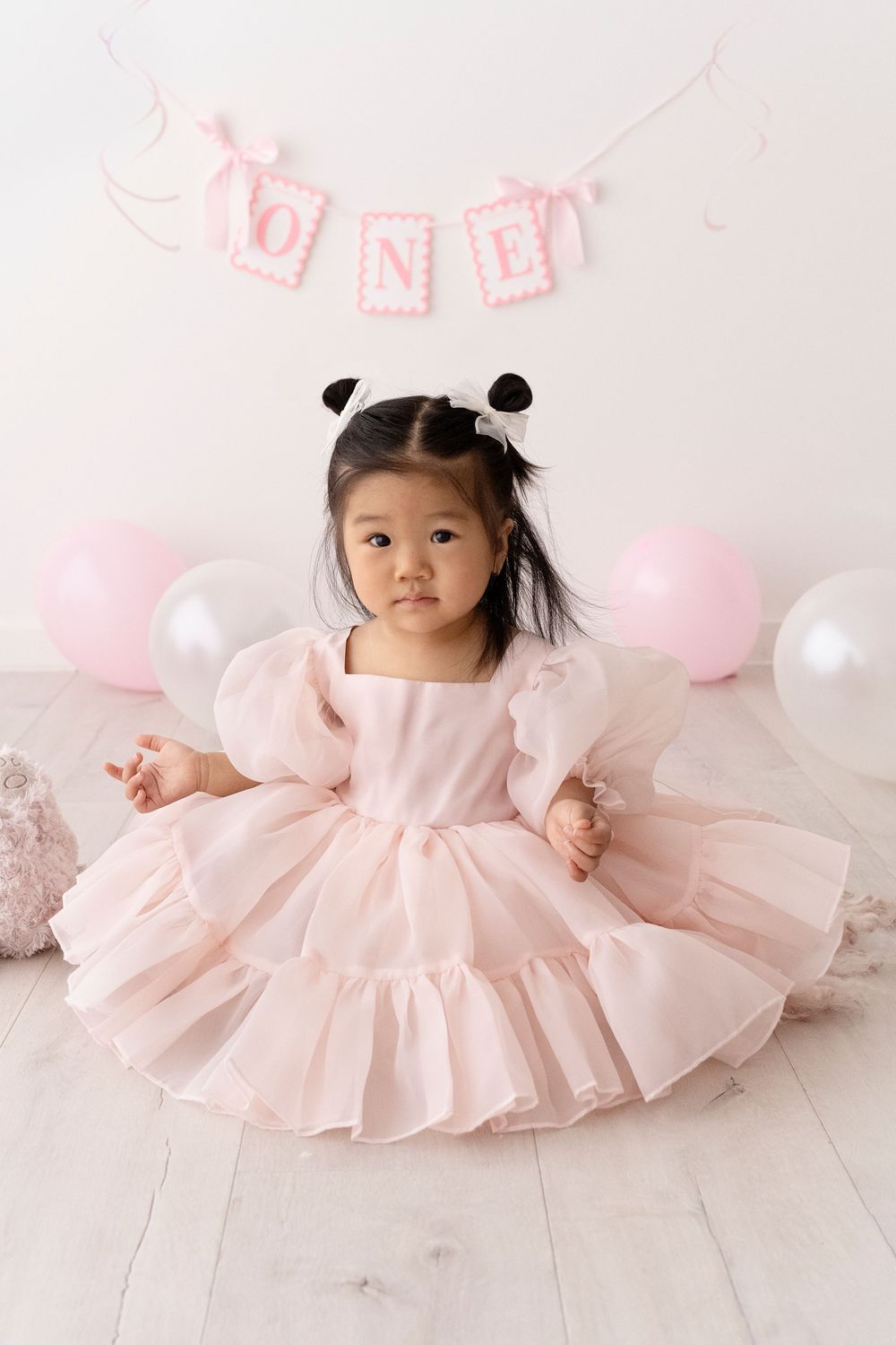 A child in a pink tulle dress sits gracefully on a white floor with pink decorations.