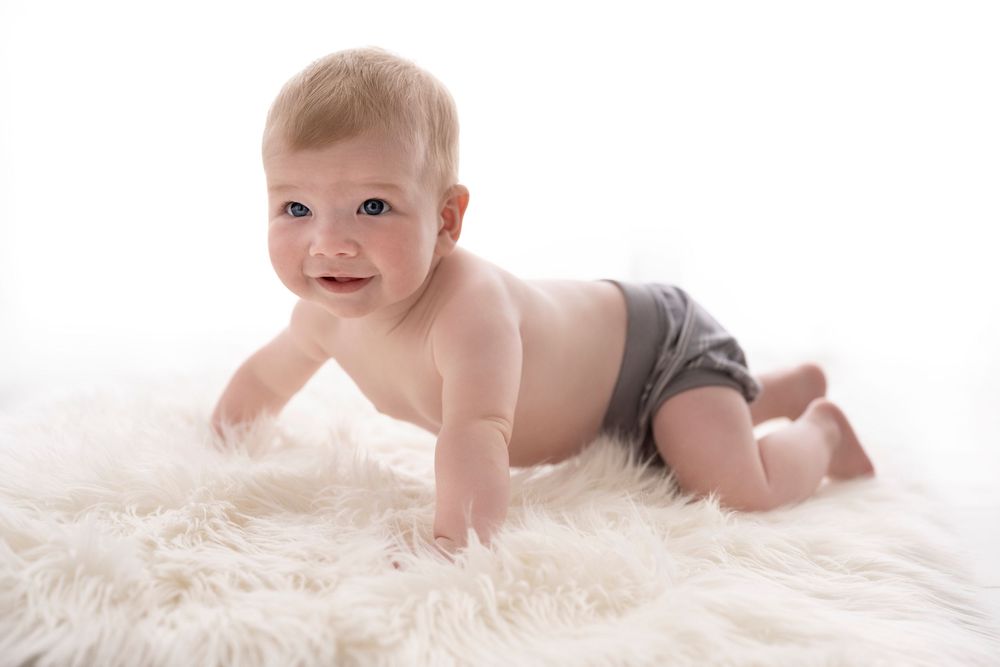 Baby Photography Melbourne, adorable baby in diaper crawls and plays on soft white fur rug in studio setting.