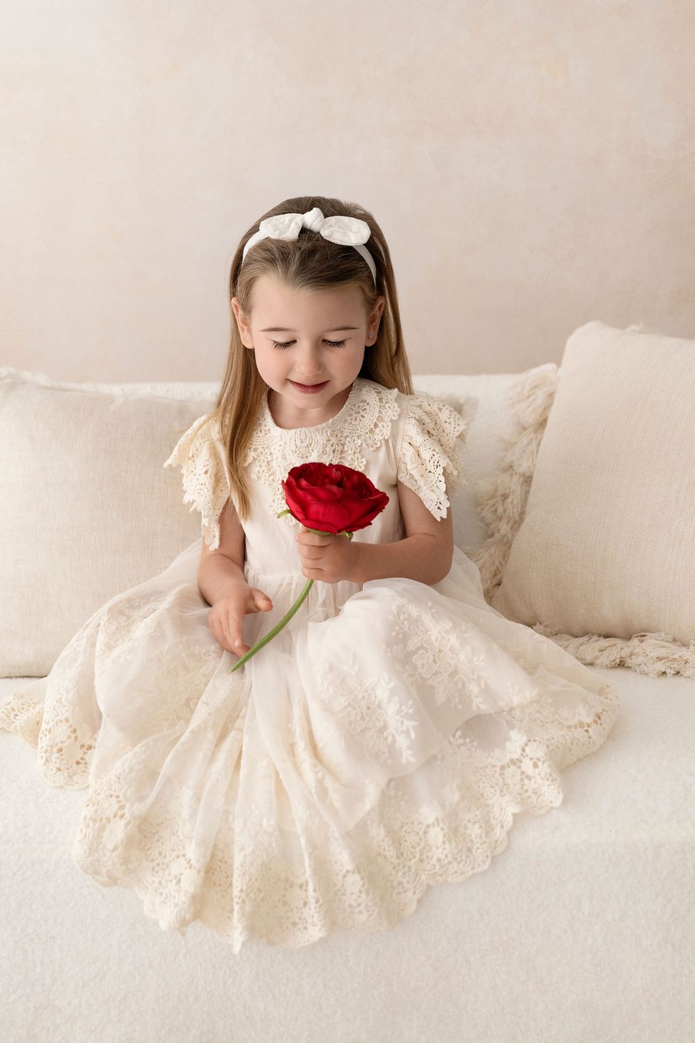 Young girl in cream lace dress holding red rose.