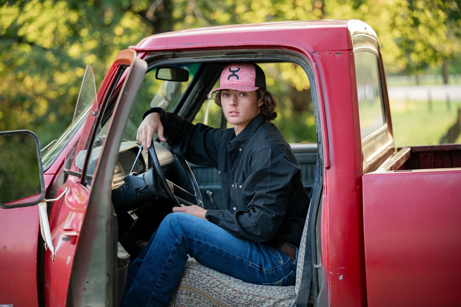 A person in a baseball cap sitting in the driver's seat of a vintage red pickup truck.