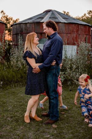 mom and dad looking at each other while daughters run around them playing