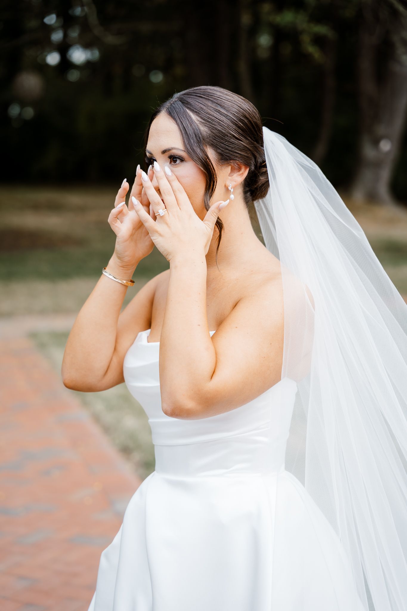 Emotional moment captured of someone in a white wedding gown and veil covering their face.