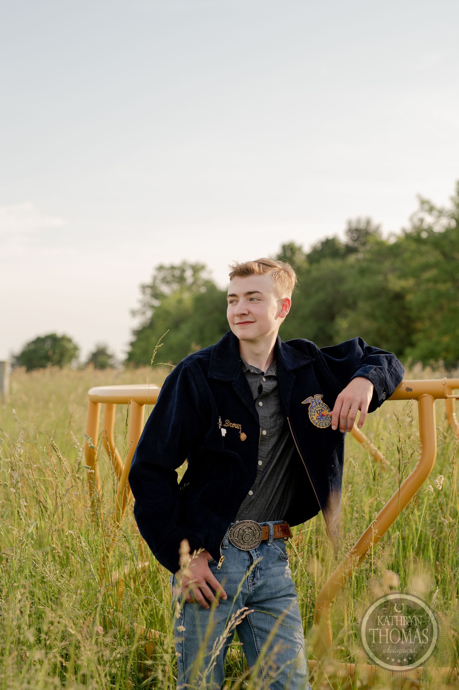 FFA member in navy jacket poses in tall grass field at sunset.