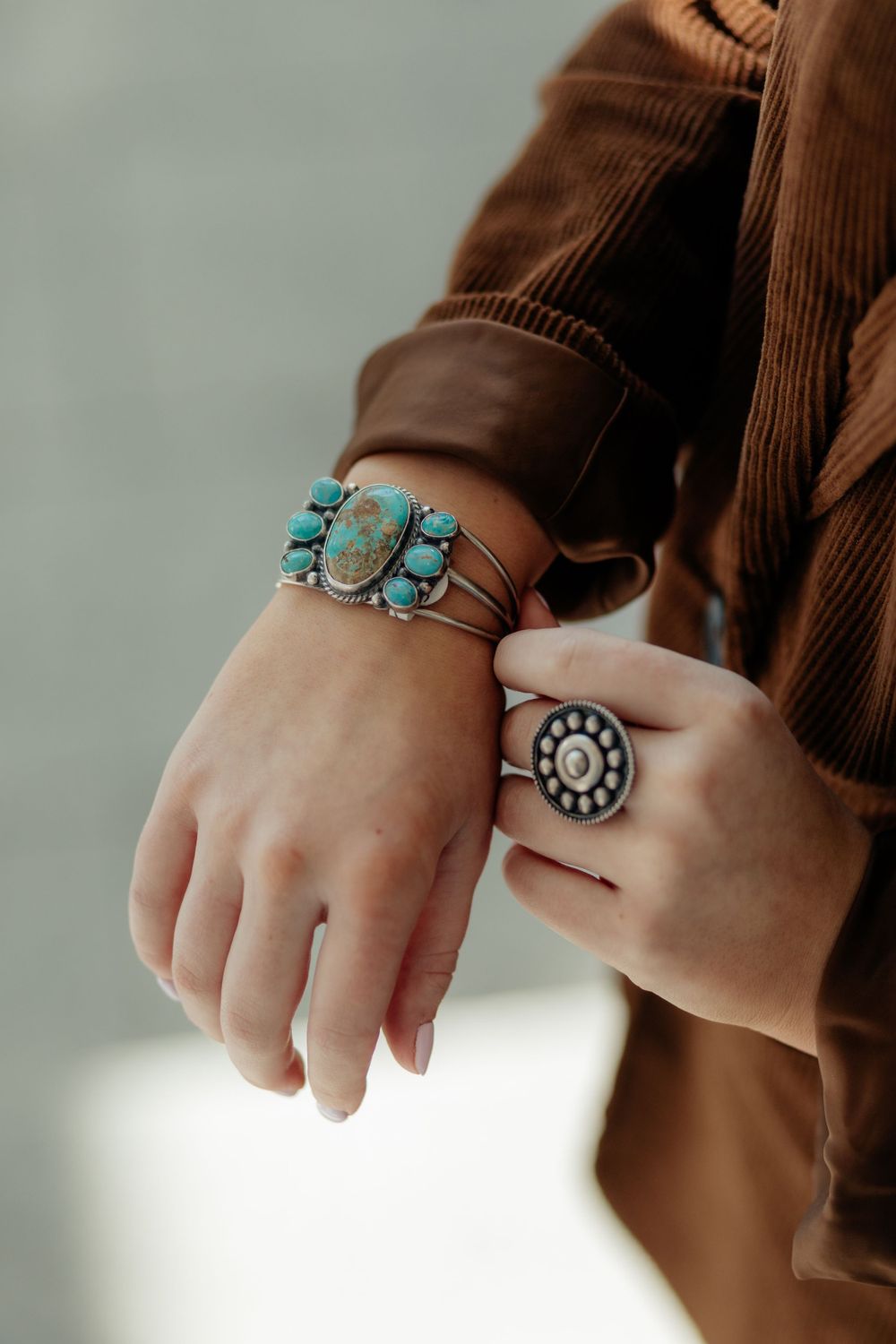 Close-up view of hands wearing southwestern style turquoise and silver jewelry with brown sweater sleeve.