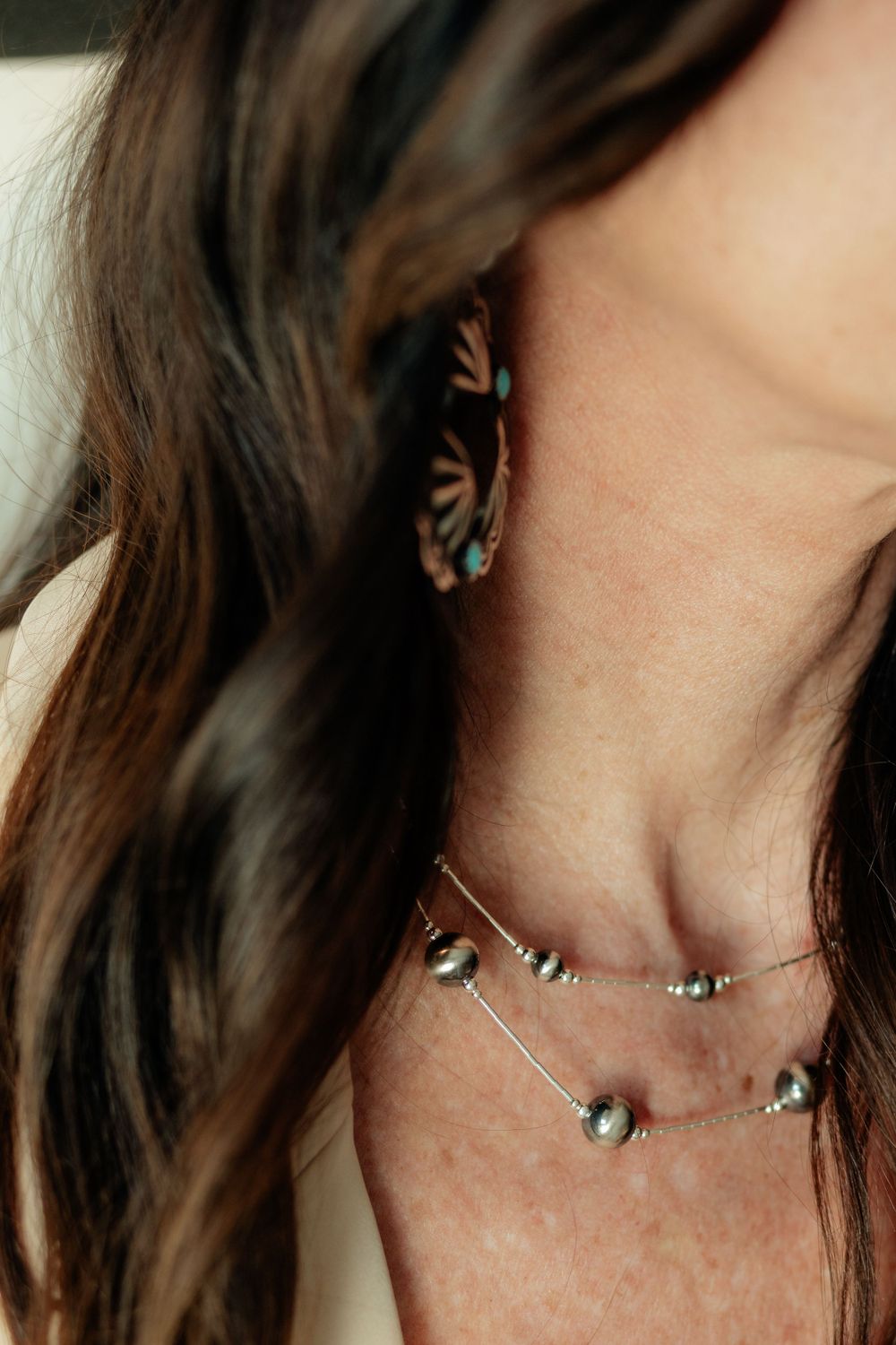 Close-up detail of layered crystal necklaces and butterfly earring against brown wavy hair and freckled skin.