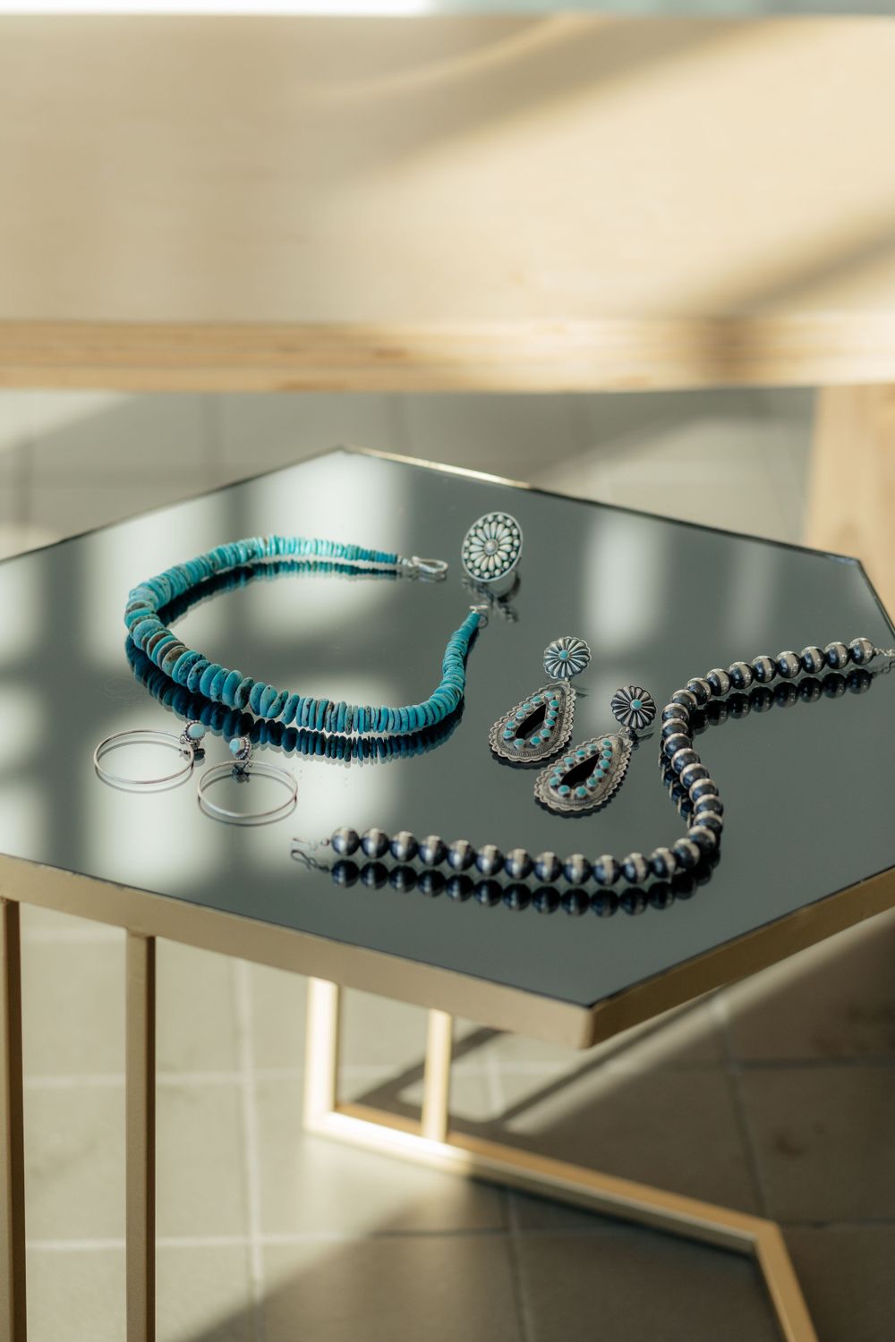 Turquoise and gray statement jewelry pieces including a beaded necklace and crescent-shaped earrings displayed on reflective surface.