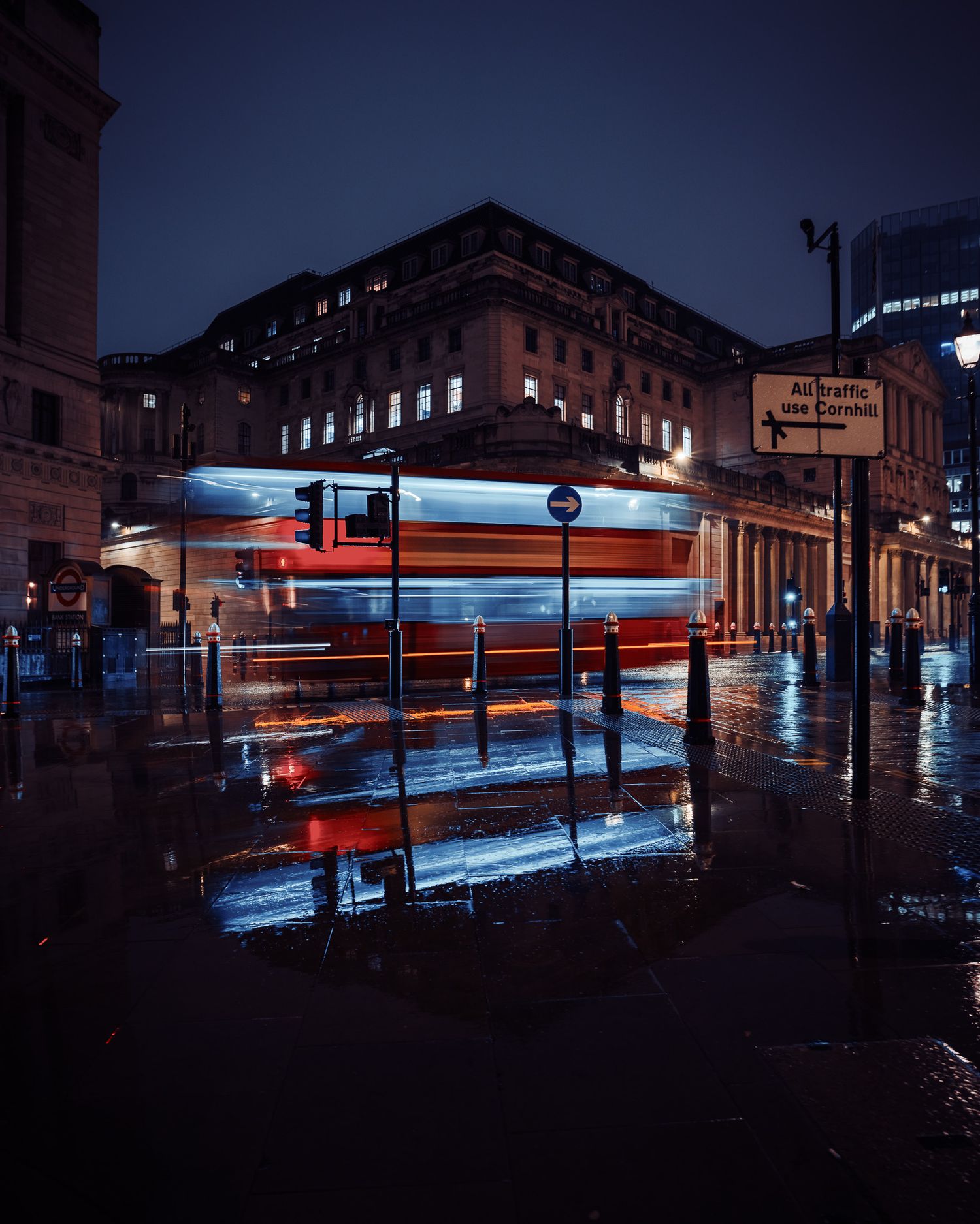 Rainy night street scene with red bus reflection in London puddles.