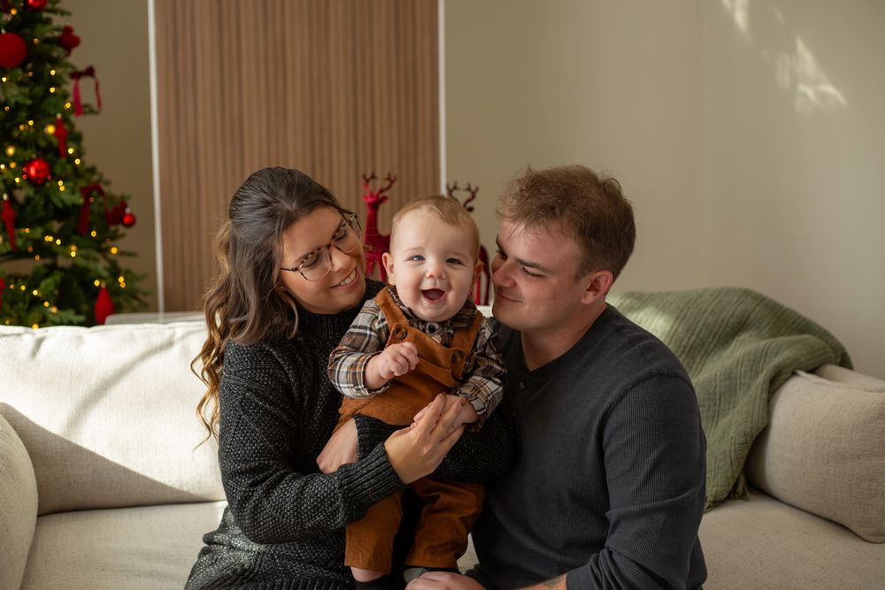 A family shares tender moments together on a couch with a decorated Christmas tree visible in the background.