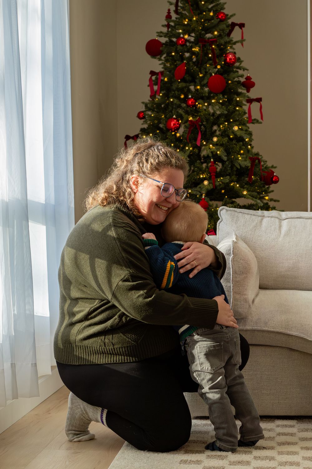 A heartwarming holiday moment in front of a decorated Christmas tree with red ornaments and twinkling lights.