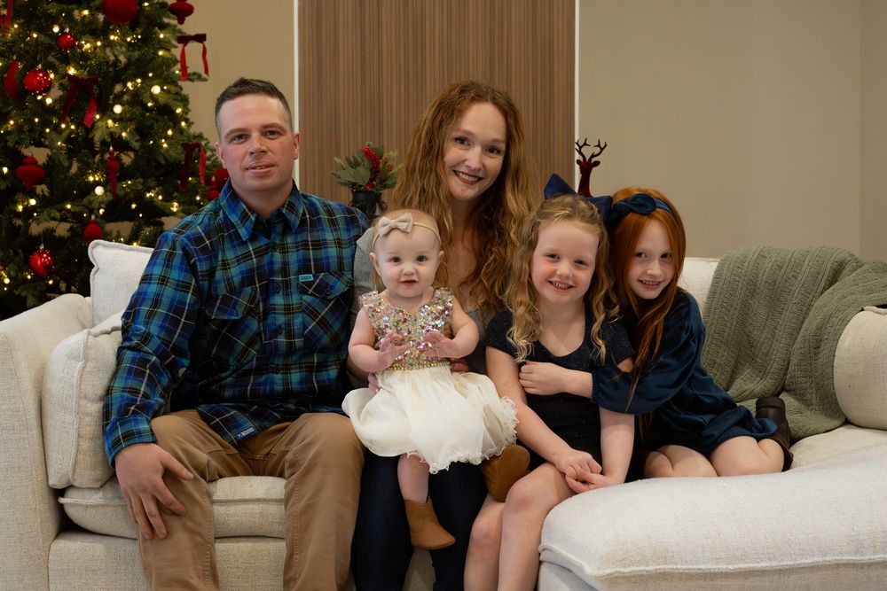 A family poses together on a beige couch with a decorated Christmas tree in the background.