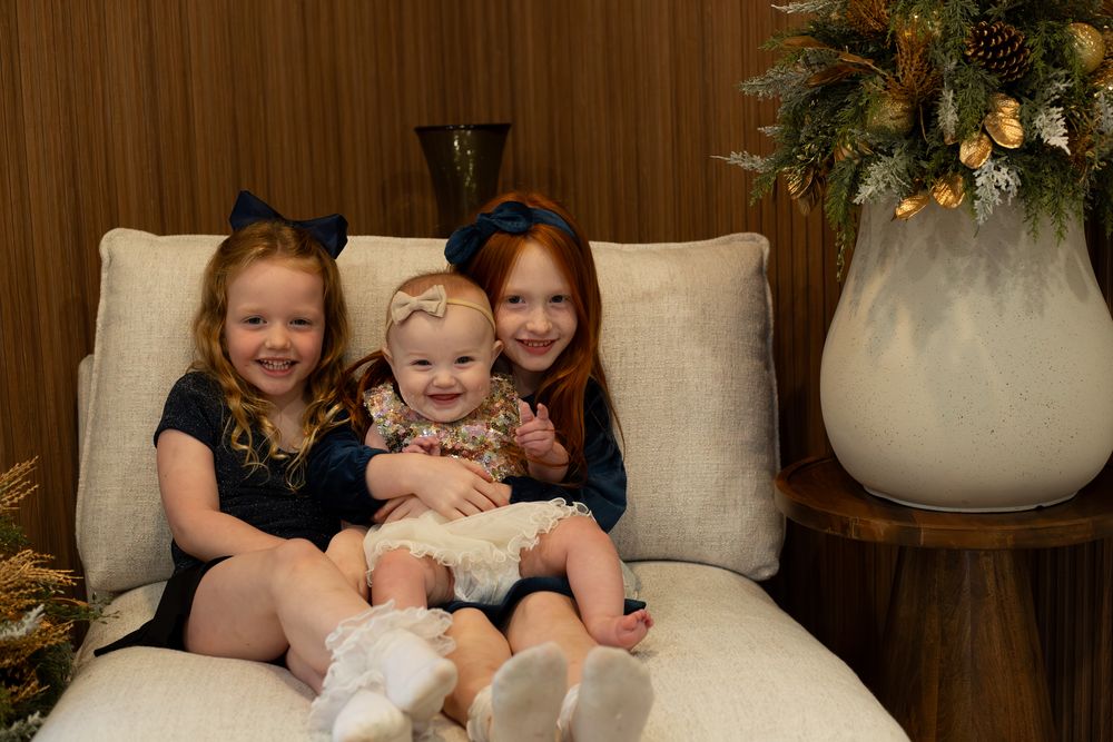 Three children sit together on a cream-colored couch with holiday decorations visible.