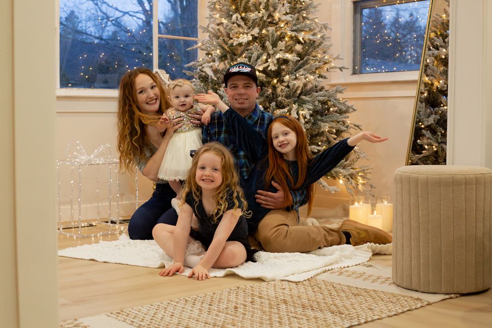 A cozy family Christmas scene with people sitting together by a decorated tree in a bright living room.