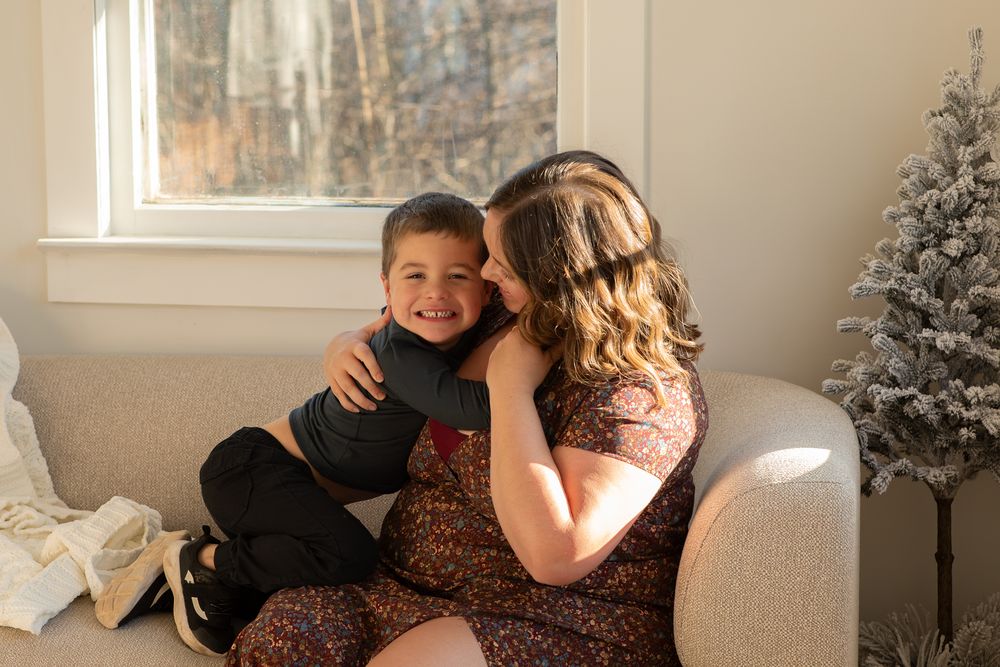 A cozy winter scene with two people sharing a tender moment on a white couch next to decorative trees.