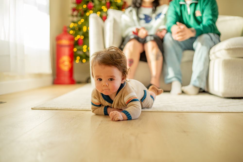 A small child peeks around the corner of a white wall in a festively decorated room during the holidays.