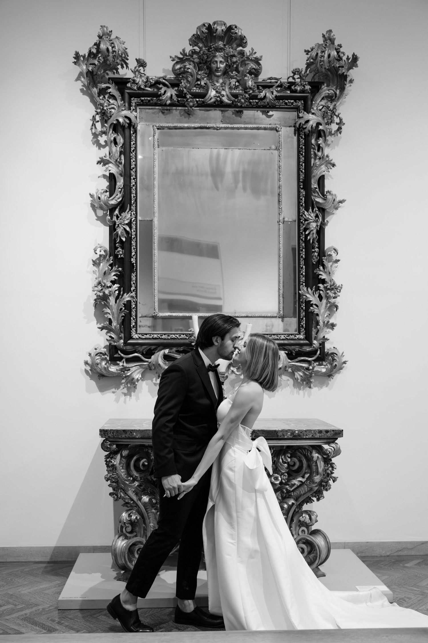 Classic black and white wedding portrait of a bride and groom kissing in front of a large ornate mirror in a museum gallery in Minnesota.