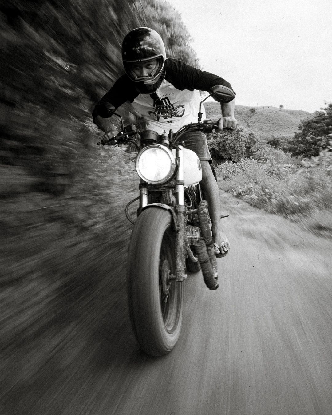 Black and white action shot of motorcycle rider racing on dirt road with motion blur effect.