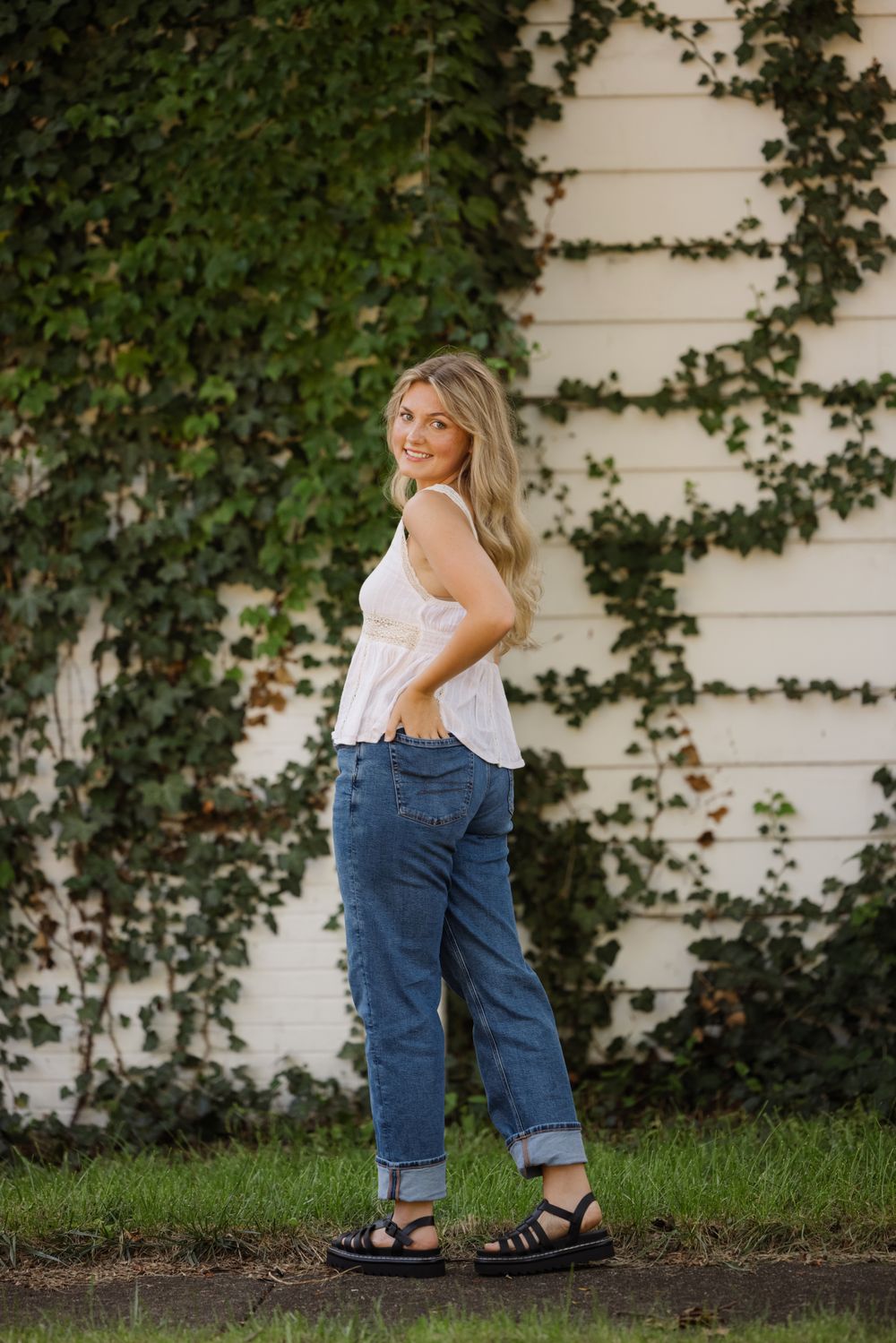 Casual outdoor portrait against a vine-covered wall wearing white top and rolled jeans.