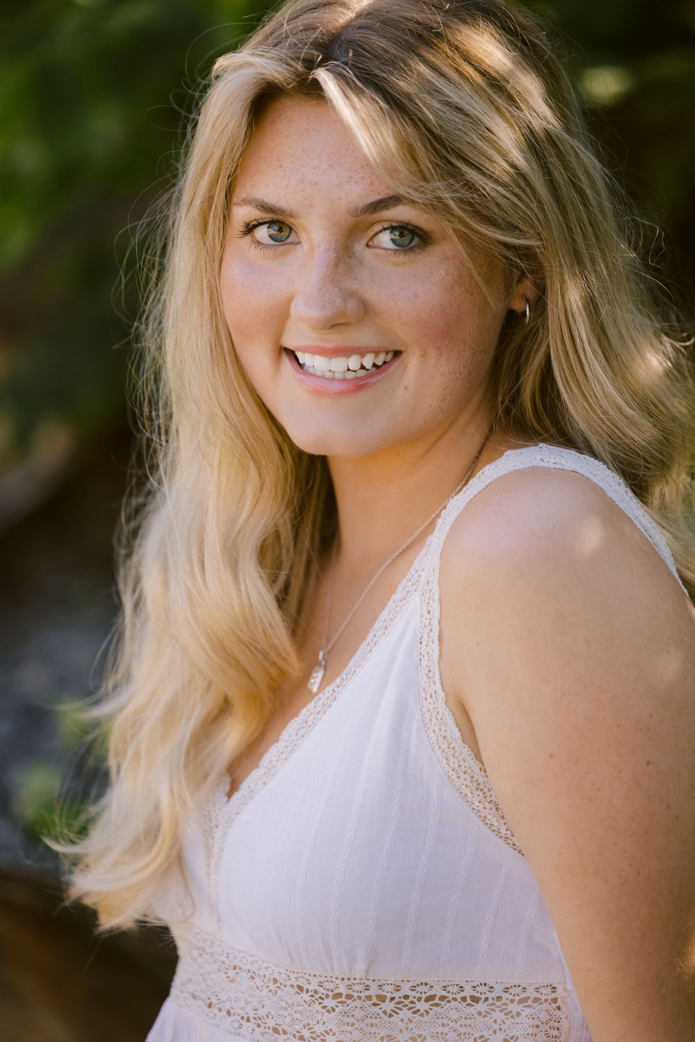 Outdoor portrait in white lace-trimmed top against natural greenery.