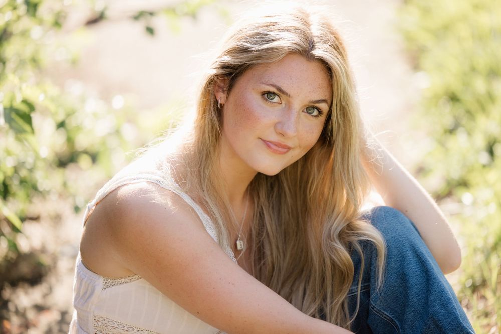 Sunlit outdoor portrait in white camisole against natural backdrop.