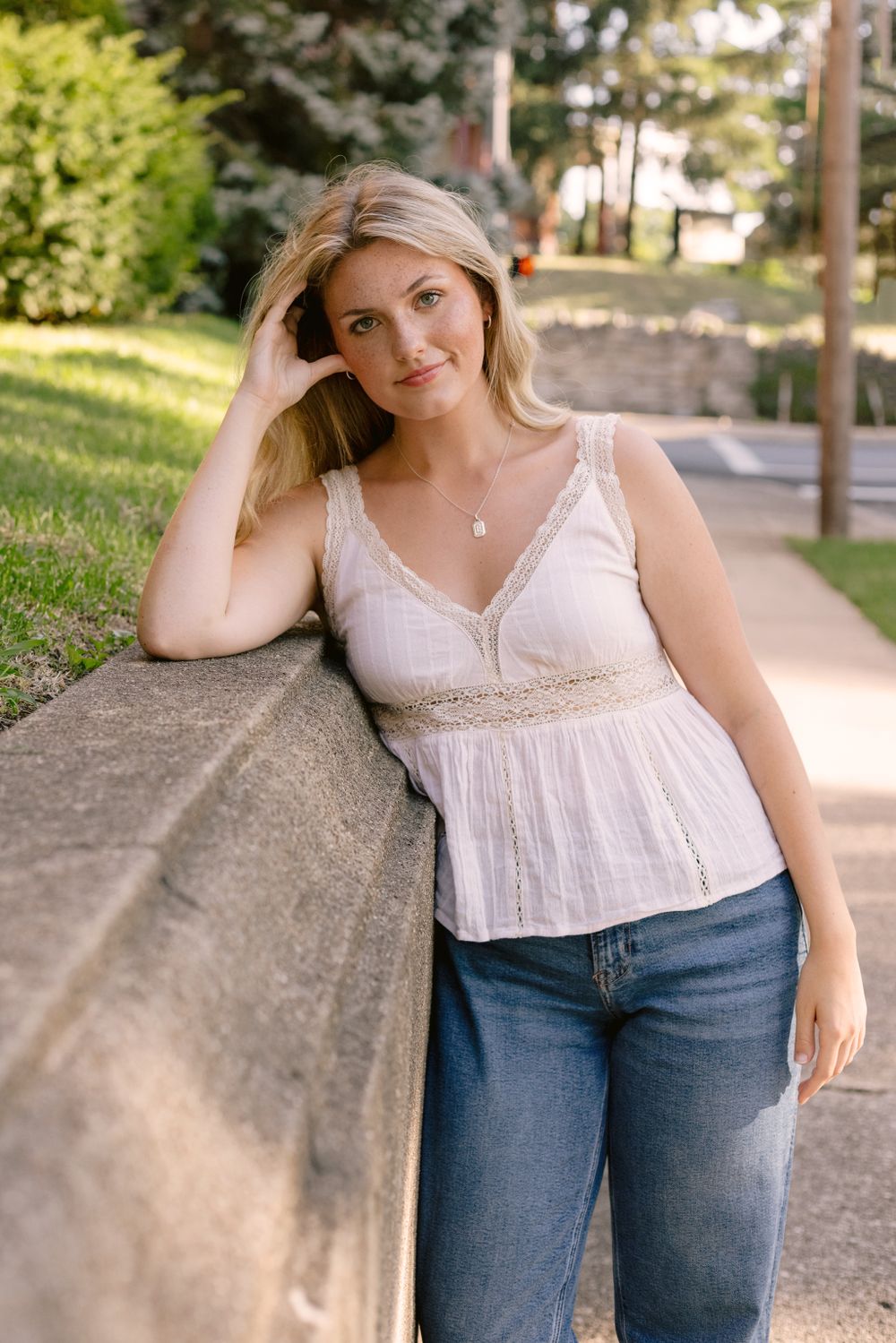 Casual summer portrait leaning against curved stone wall in afternoon light.