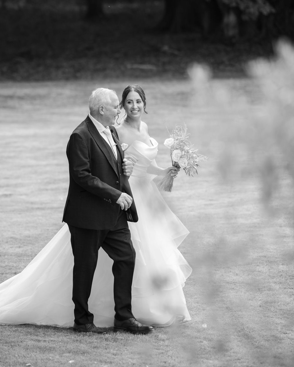 A black and white wedding photo showing a couple walking together in a misty outdoor setting.