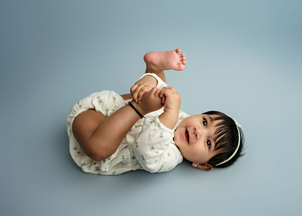 A baby wearing white lace clothing poses on a soft blue studio background.