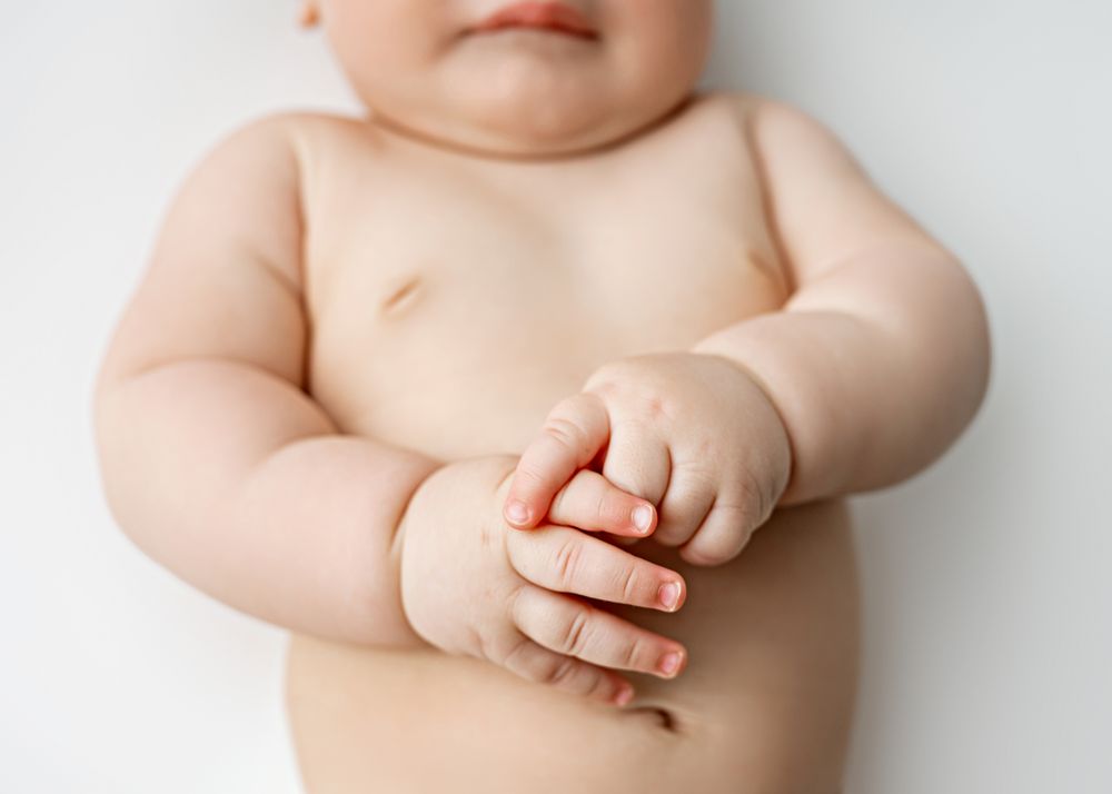 Close up view of baby's torso and clasped hands against white background.