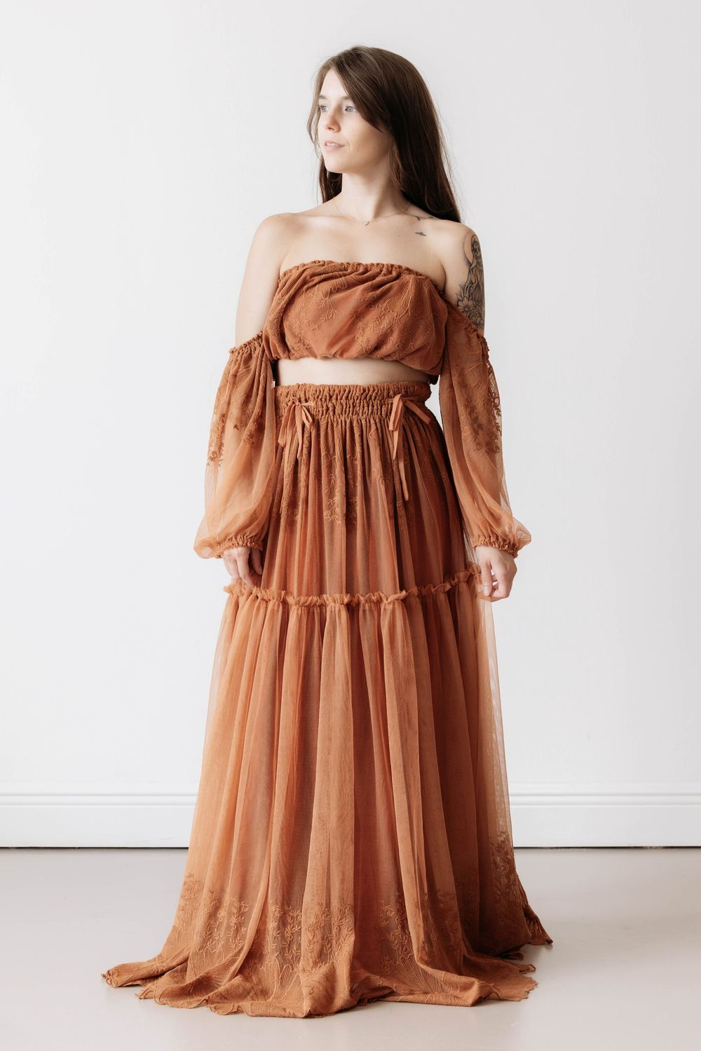 Woman wearing a rust brown boho off-shoulder crop top and flowing tiered maxi skirt set with lace trim details.