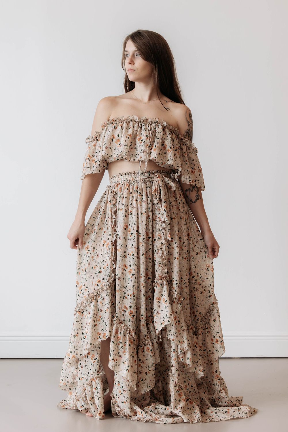 Woman wearing a floral off-shoulder crop top and matching maxi skirt set in beige with colorful floral print.