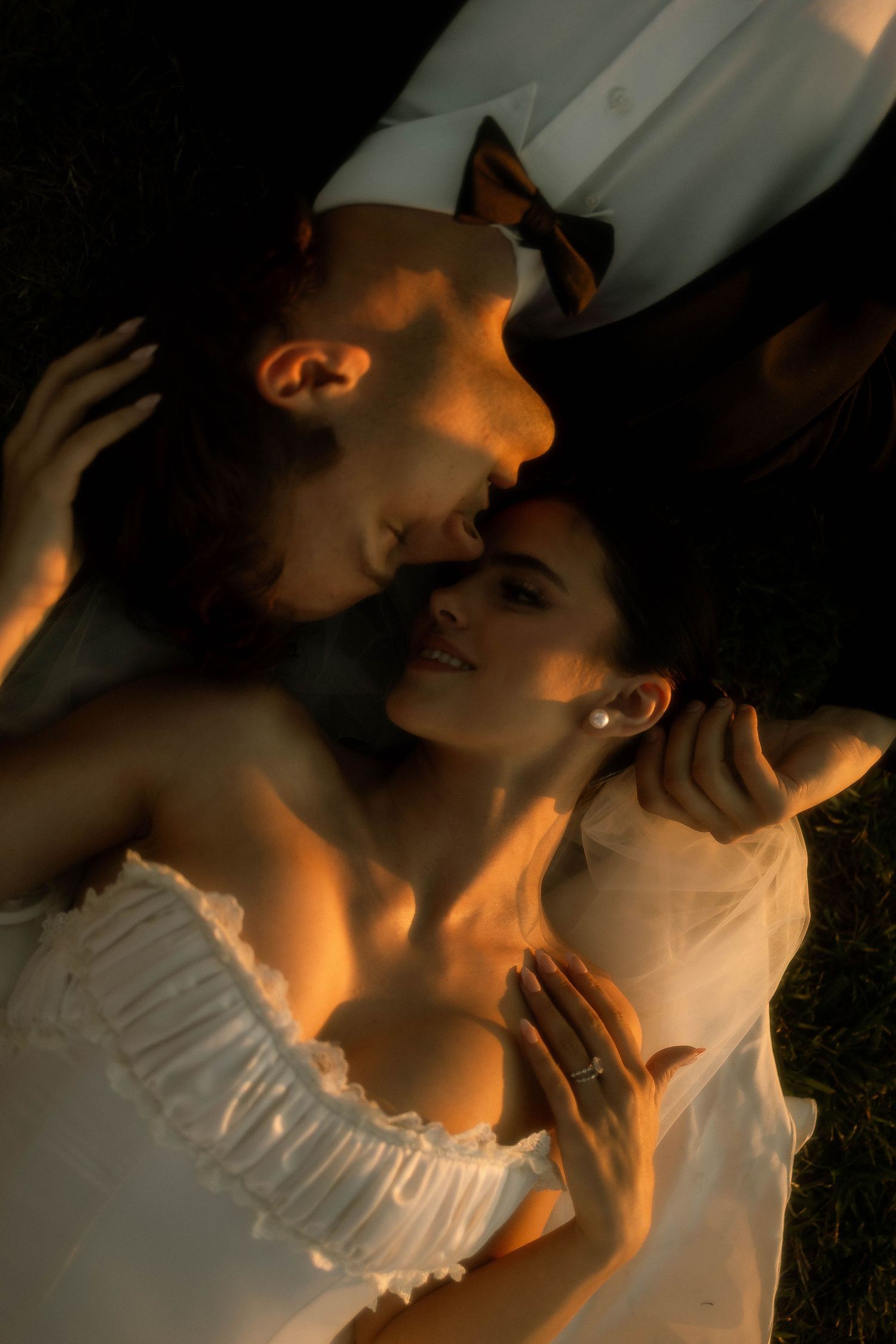 Bride in white strapless wedding gown with groom's hand on her waist, warm golden light photography.