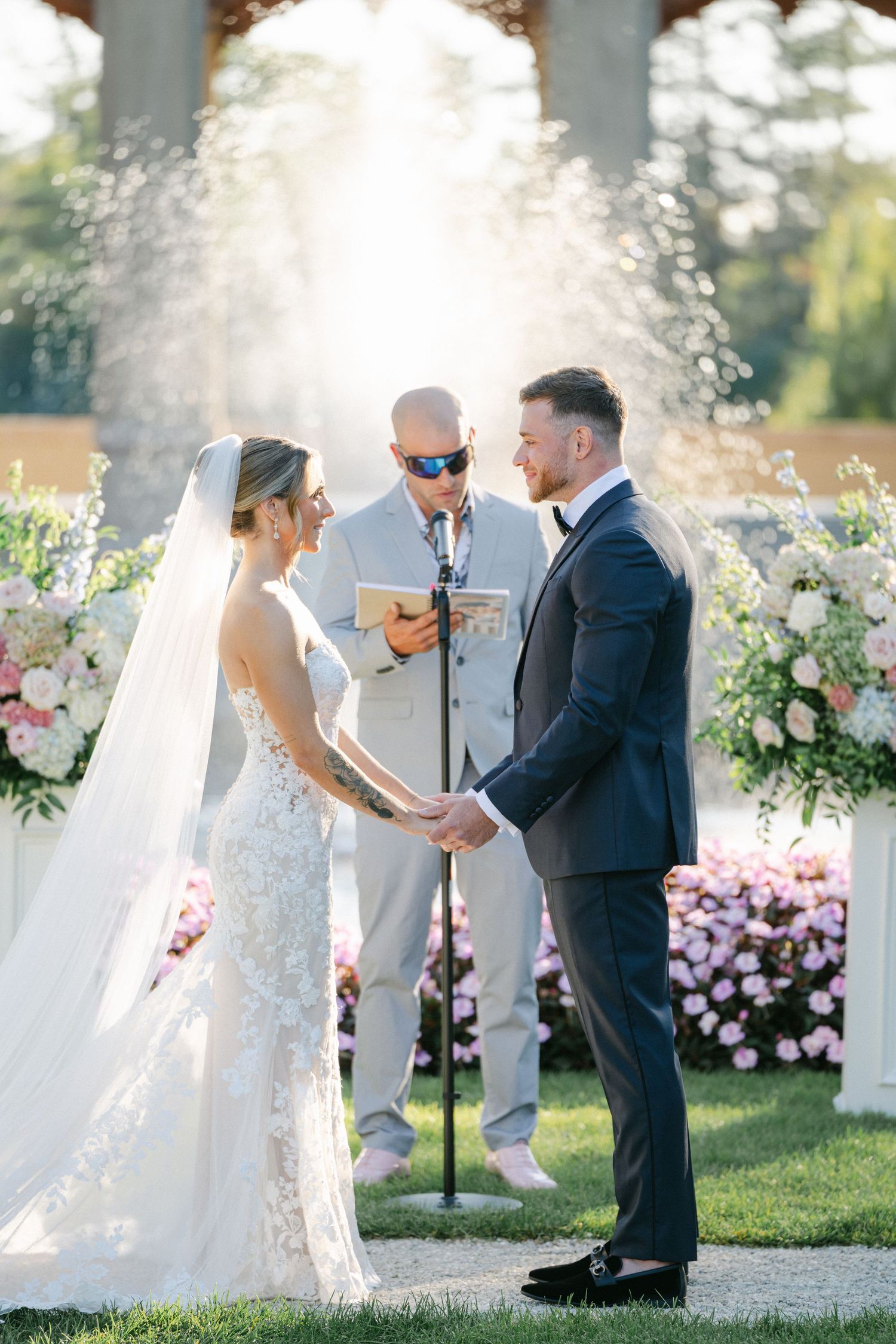Armour House Wedding - Bride and groom exchange vows outdoors at elegant wedding ceremony with pink floral arrangements.