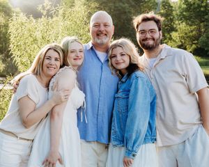 Happy family of five smiling together outdoors in a lush green setting during golden hour.
