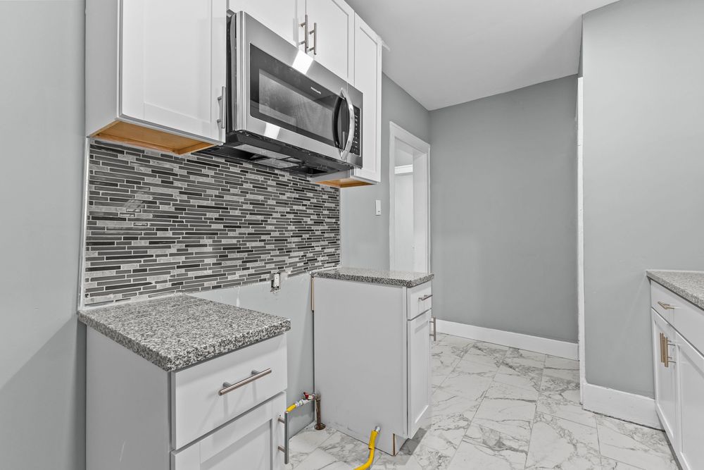 Modern kitchen with white cabinets, granite countertops, mosaic tile backsplash, and stainless steel microwave. Detroit Michigan