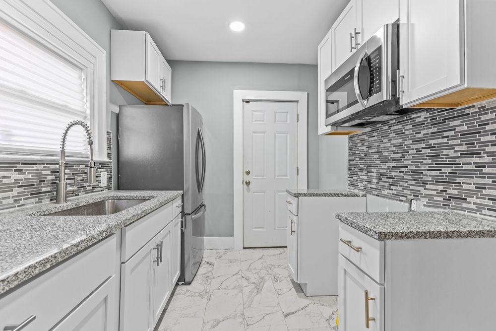 Modern kitchen with white cabinets, granite countertops, stainless steel appliances, mosaic tile backsplash, and marble floors. Detroit Mich