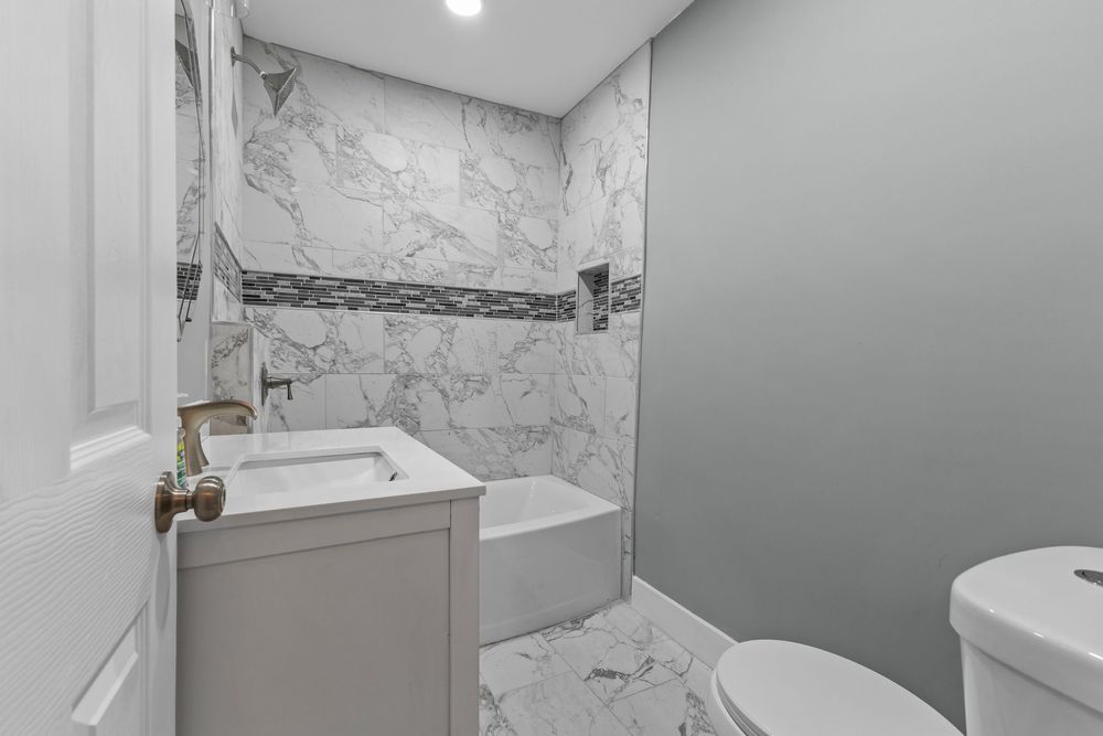 Modern bathroom with marble tile walls, tub-shower combo, white vanity, and toilet. Detroit Michigan
