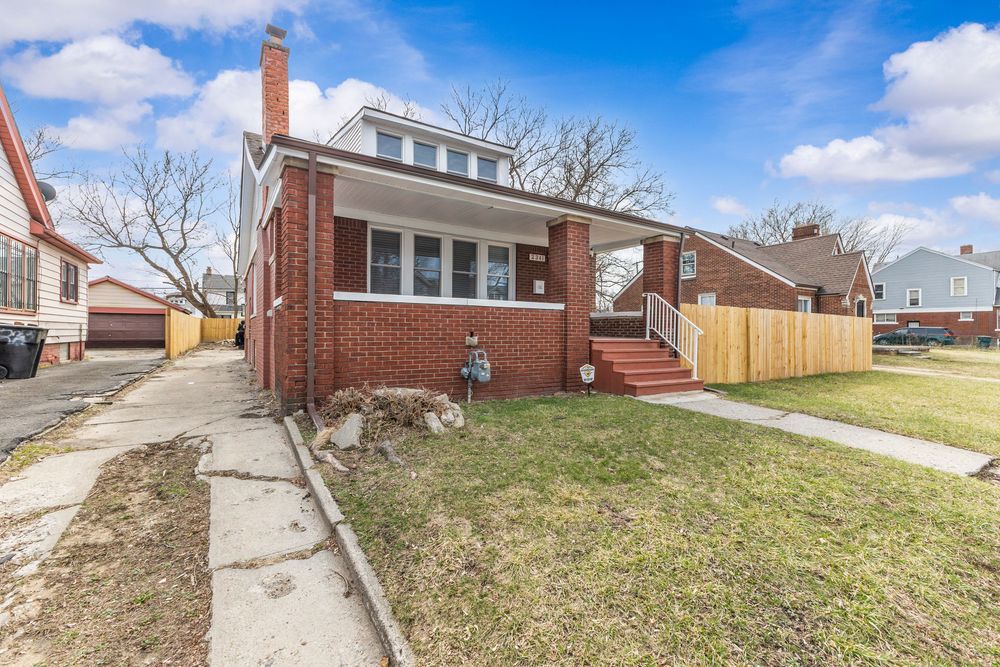 Brick bungalow home with covered porch, wood fence, and manicured lawn on a quiet residential street. Detroit Michigan