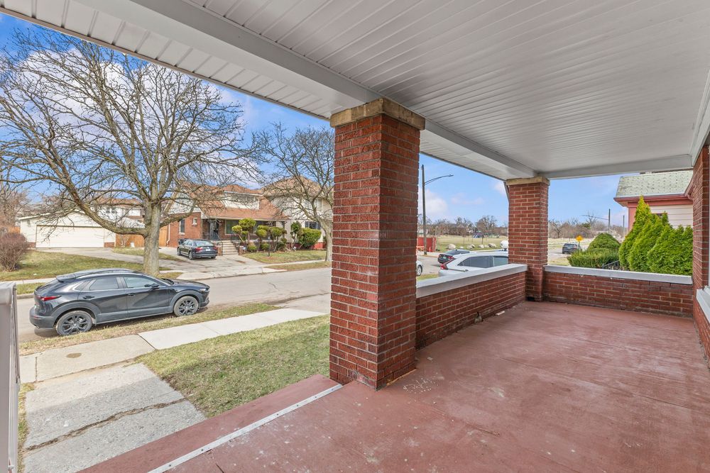Covered brick front porch with red tile flooring overlooking a quiet suburban neighborhood street with parked cars. Detroit Michigan