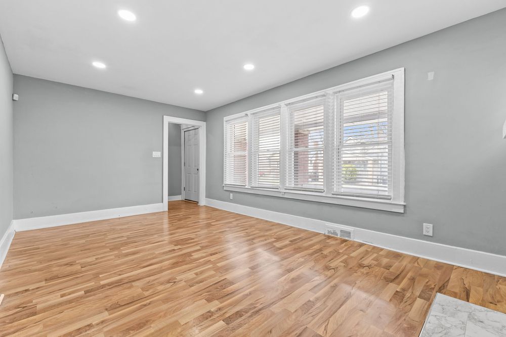 Bright empty room with light hardwood floors, gray walls, white trim, recessed lighting, and a white-framed window. Detroit Michigan