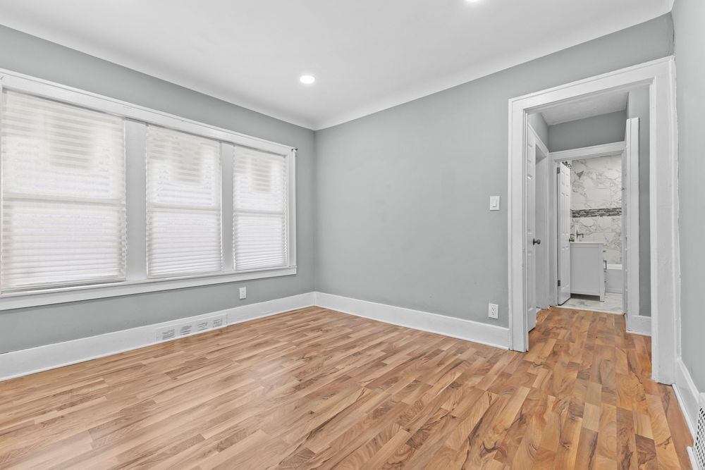 Empty bedroom with light hardwood floors, gray walls, crown molding, and an en-suite bathroom. Detroit Michigan