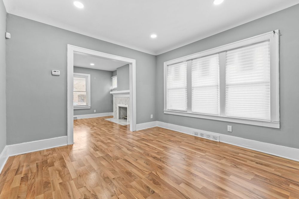 Bright living room with hardwood floors, gray walls, crown molding, and a white fireplace.