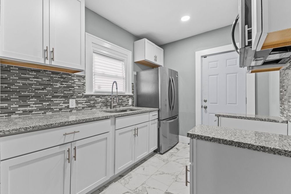 Modern kitchen with gray cabinets, granite countertops, stainless steel fridge, mosaic backsplash, and marble tile floors. Detroit Michigan