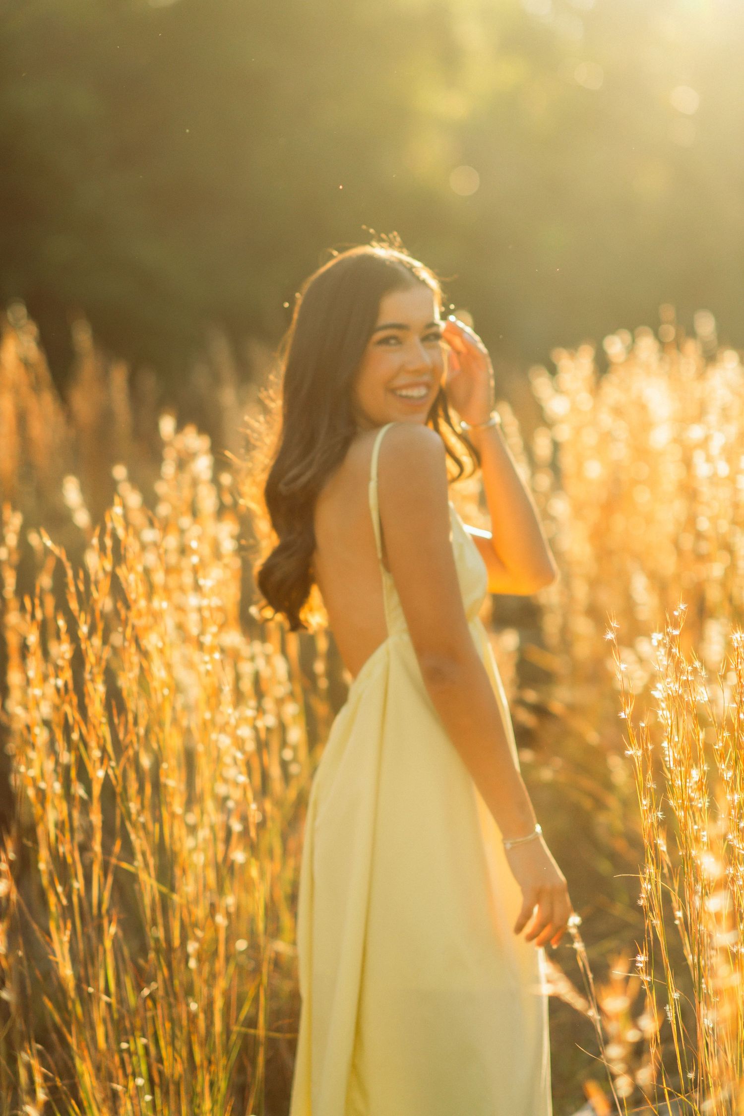 Young woman in yellow sundress smiling in golden sunlit field.