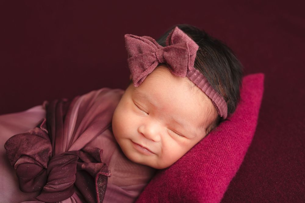newborn photography session Sammamish WAon a burgundy pillow with pink swaddling.