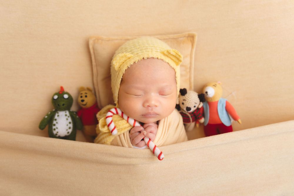 newborn photography session Sammamish WA in yellow bonnet nestled among plush toys and stuffed animals in beige backdrop.