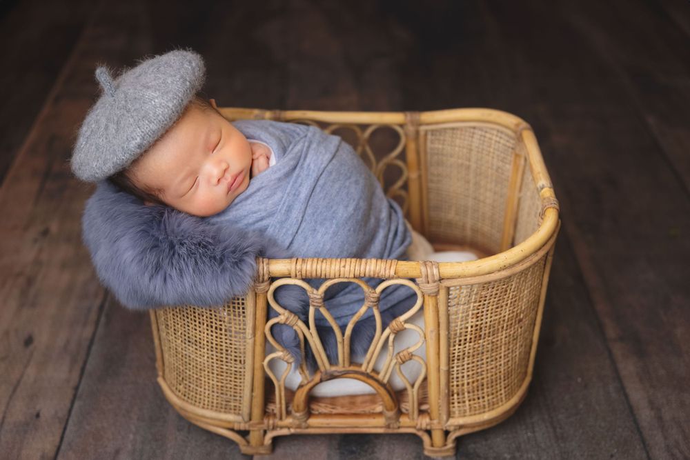 newborn photography session Sammamish WA in blue fabric inside a vintage wicker bassinet on wooden floor.