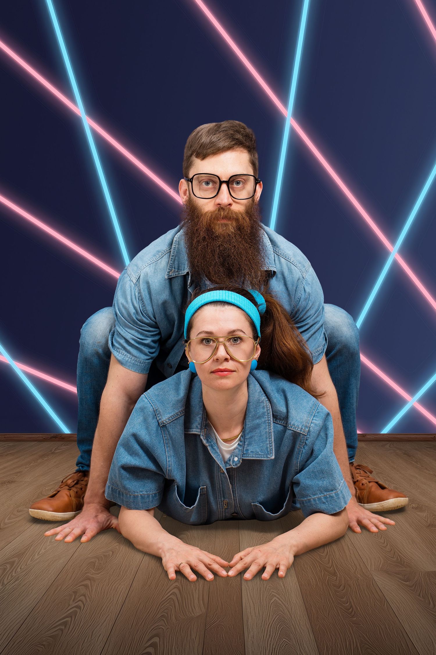 Awkward 80's photo of a man and woman wearing double denim, where man is posing like a frog on top of the woman with a neon laser backdrop