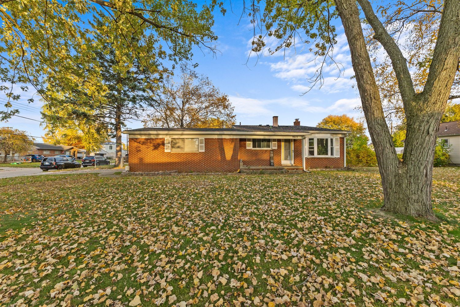 Brick ranch home surrounded by mature trees with autumn leaves covering the front yard.